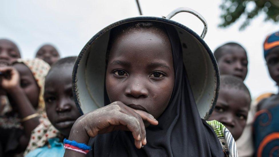 A young girl with a pot on her head poses with other children at one of the Internally-Displaced People (IDP) camps Gwoza, north-eastern Nigeria, on August 1, 2017