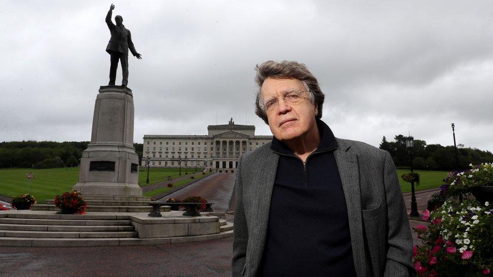 Caption: Merlin Holland, grandson of Oscar Wilde, at the statue of Edward Carson outside Parliament Buildings in Belfast, during filming for Edward Carson And The Fall Of Oscar Wilde