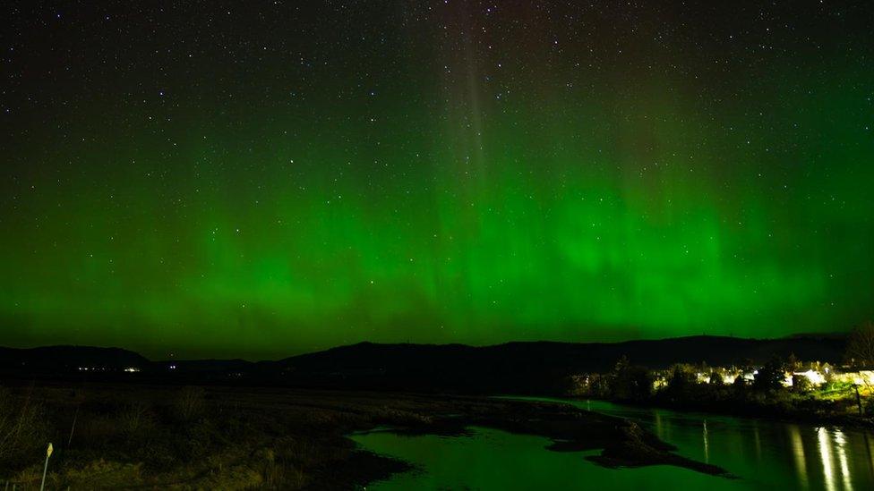 Green filled sky with the shining of night lights in the distance.