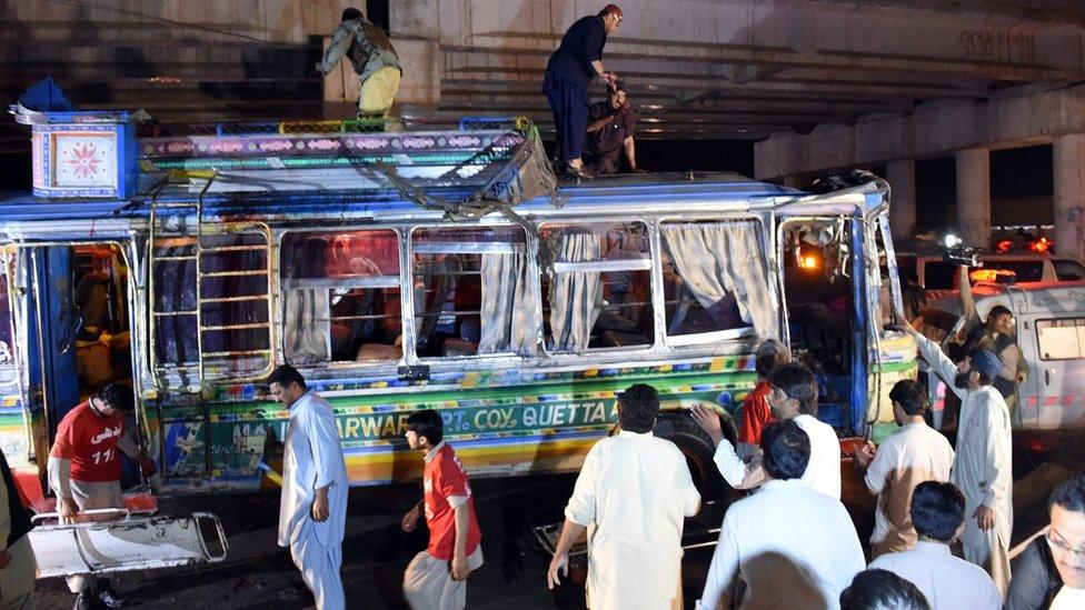 Pakistani volunteers and residents gather beside a damaged bus after a bomb explosion in Quetta on October 19, 2015