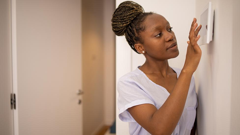 Woman adjusting thermostat on the wall with door in background