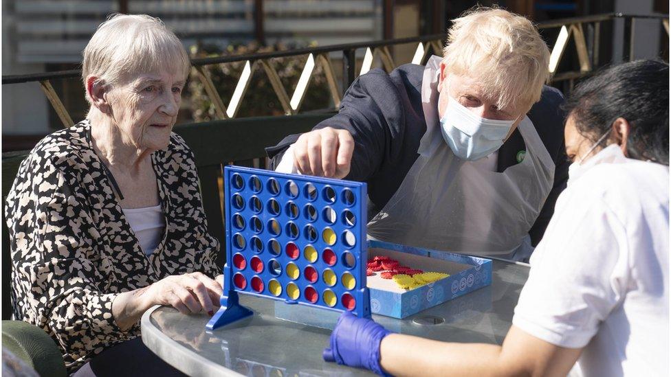 Prime Minister Boris Johnson plays Connect 4 with resident Janet (L) and carer Lakshmi during a visit to Westport Care Home in Stepney Green