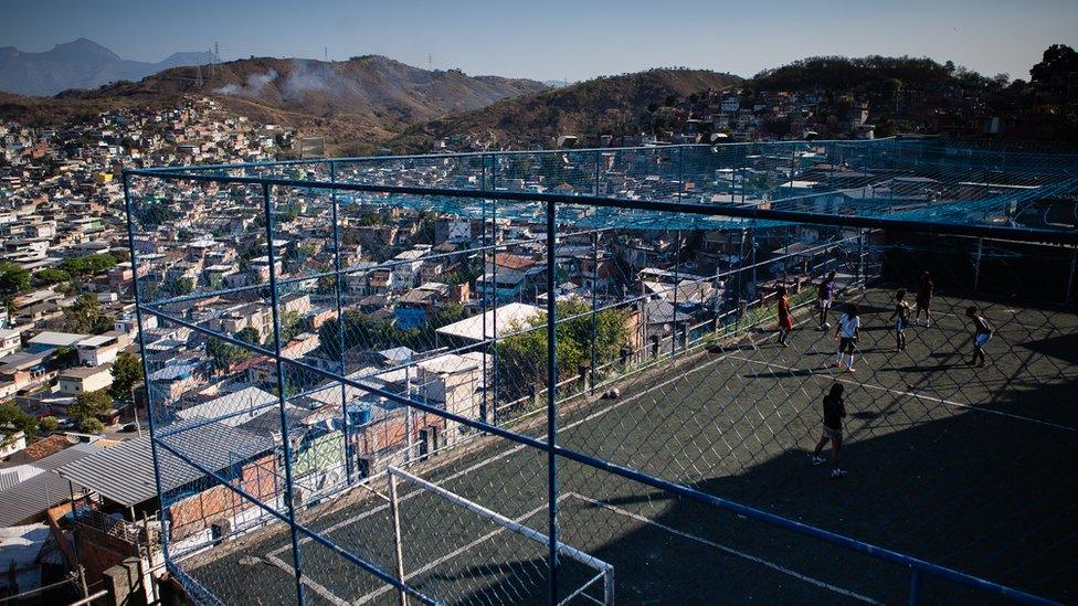 A view of the caged football pitch as the girls train, with a sweeping view of the hilly favela shanty town landscape visible beyond it