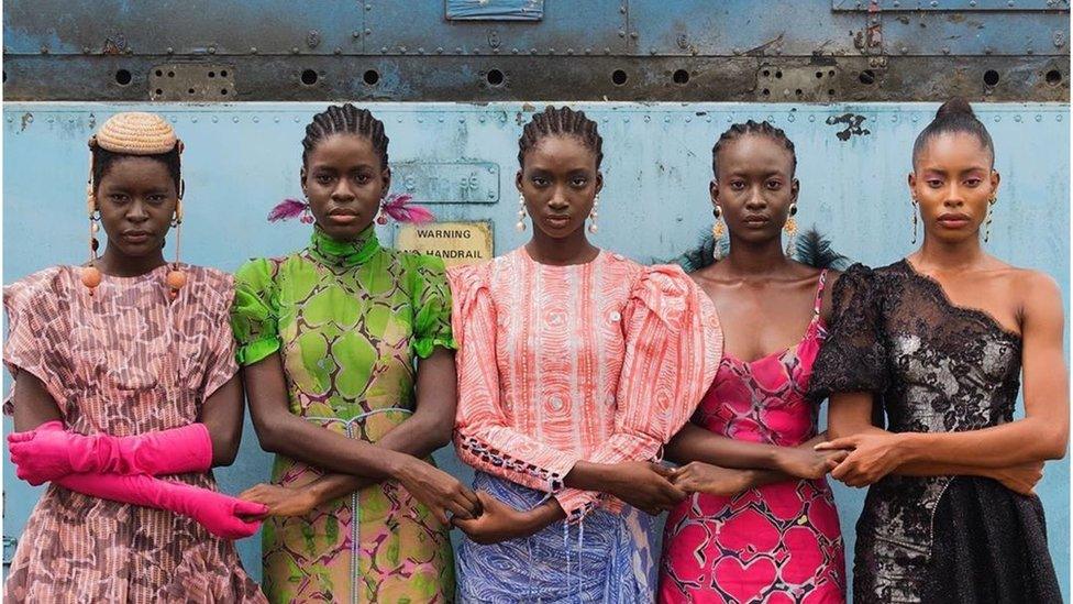 Five models holding hands, they are wearing colourful clothing