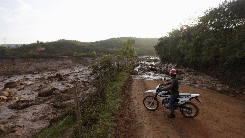 A man on a motorbike inspects the mud across the road.