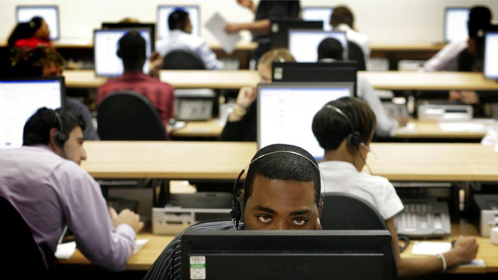 Call centre workers sitting at desks with computers and handsets