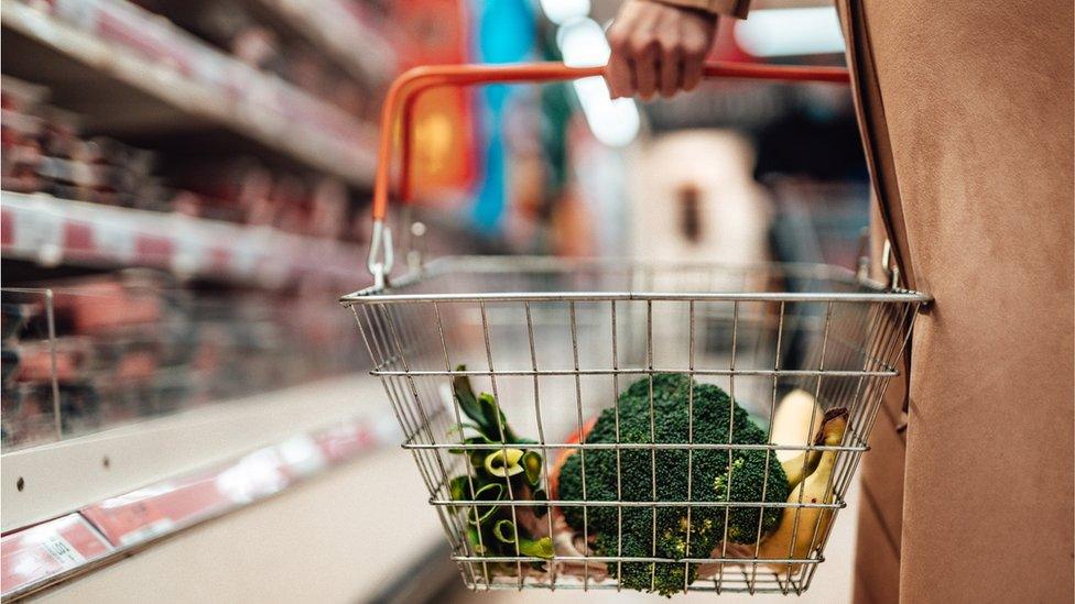 A woman holds a shopping basket containing vegetables in a supermarket