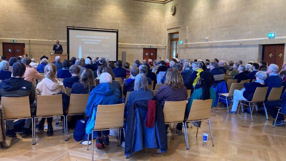 A hall filled with people sitting down, listening to a guest speaker