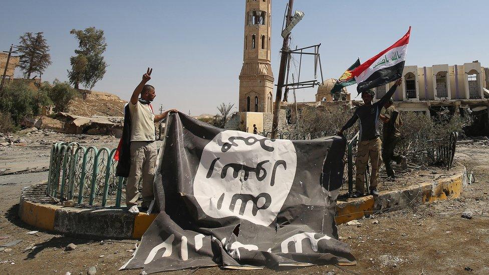 Fighters from the Hashed al-Shaabi (Popular Mobilisation units), backing the Iraqi forces, pose with a flag of the Islamic State (IS) group in Tal Afar on 27 August 2017