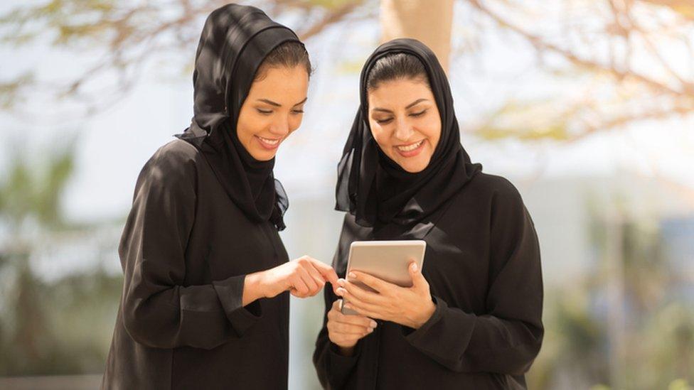 Two Abaya-wearing women looking at a tablet