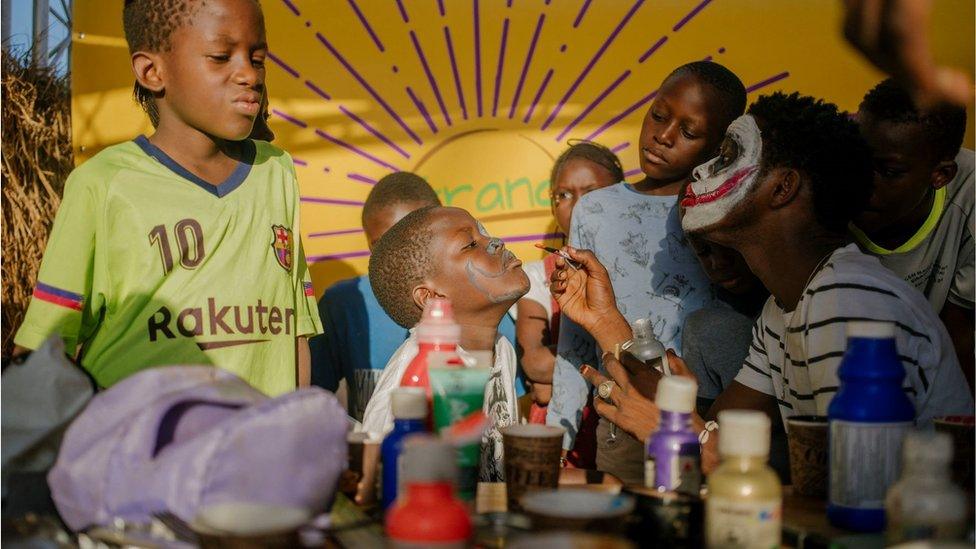 A child getting is face painted by another child.