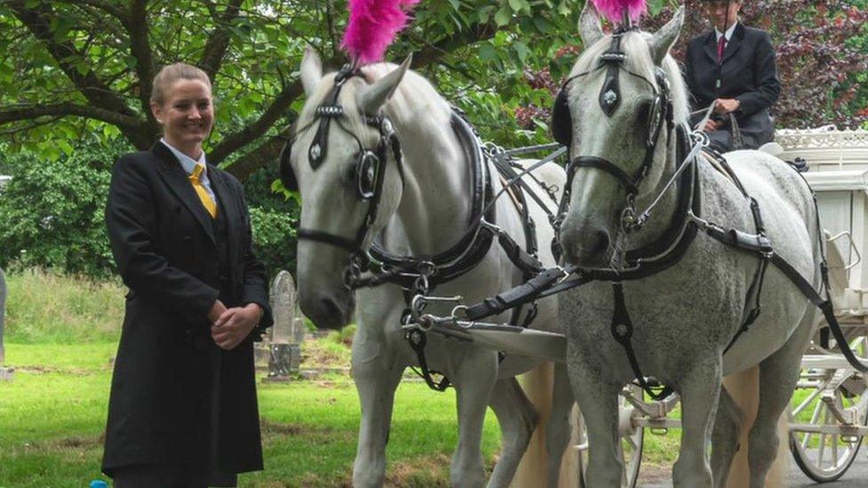 Ayesha Slader in funeral director's outfit next to two horses