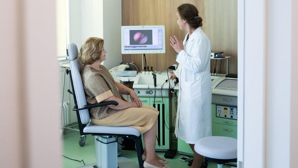 A woman sat down and a doctor standing by a scan machine in a hospital