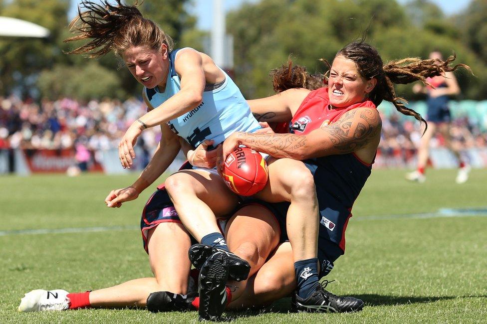 Three femeale players clash over a football