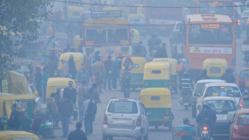 Indian commuters travel on a polluted road near a bus terminus in the Anand Vihar District of New Delhi.