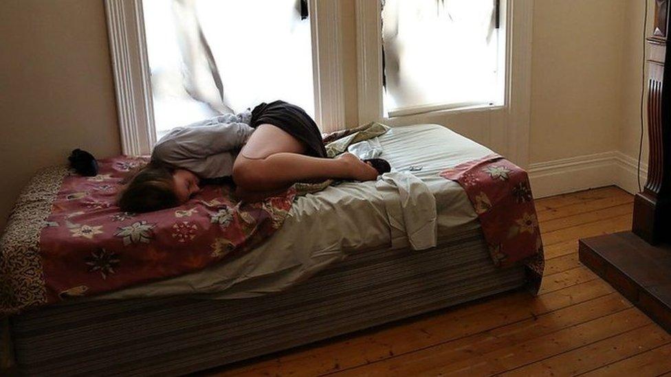 A woman sheltering on a bed looking scared