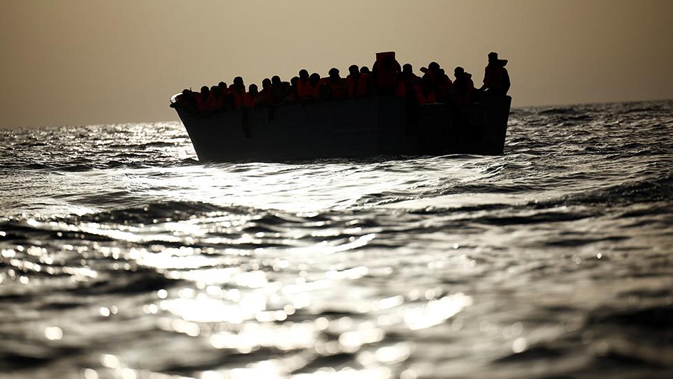 Migrants (in silhouette) wait in a boat during a search and rescue (SAR) operation by the NGO Proactiva Open Arms Uno rescue boat in central Mediterranean Sea, August, 17, 2022.