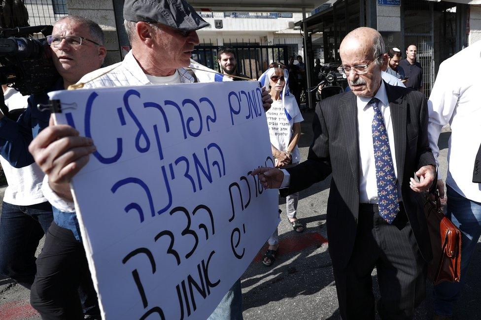 Benjamin Netanyahu's lawyer, Ram Caspi (right), walks past a man carrying a poster saying "We support the state prosecutors and the justice system", as he arrives at the Israeli justice ministry in Jerusalem (2 October 2019)