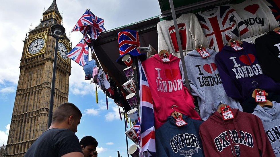 Tourists look at London-themed merchandise near the Big Ben clock face and the Elizabeth Tower at the Houses of Parliament in central London