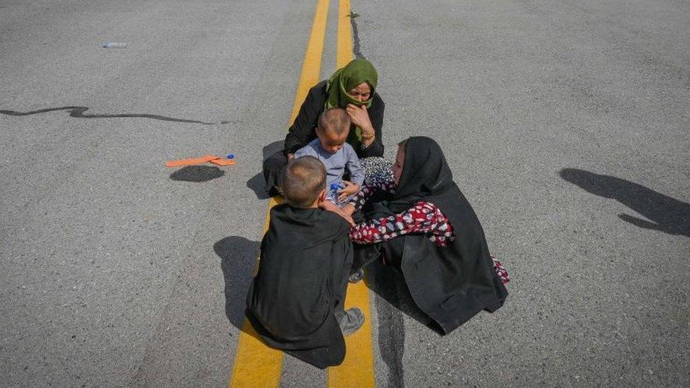 Afghan people sit along the tarmac as they wait to leave the Kabul airport