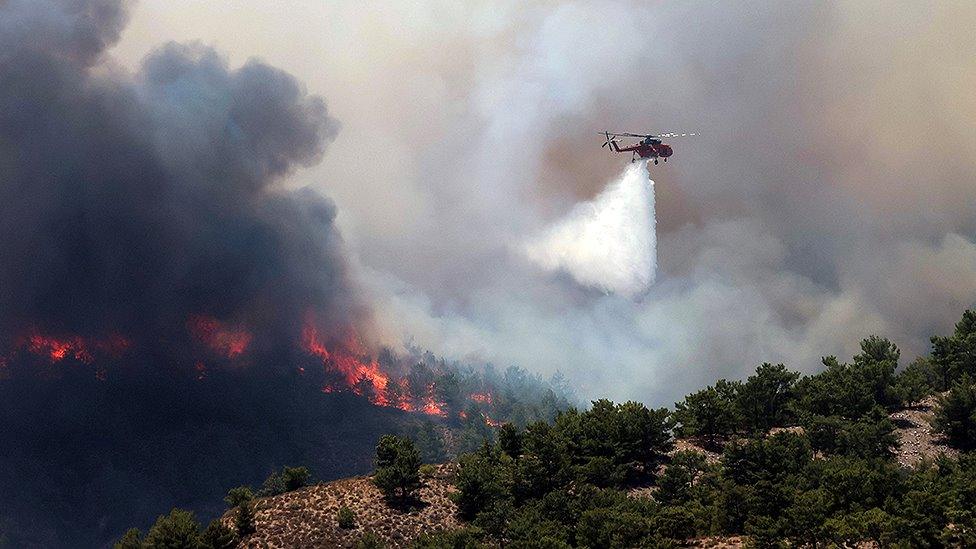 A firefighting helicopter makes a water drop as a wildfire burns near the village of Archangelos, on the island of Rhodes