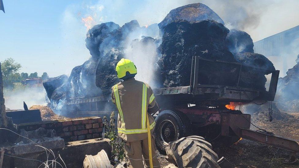 A firefighter damping down burning bales of straw