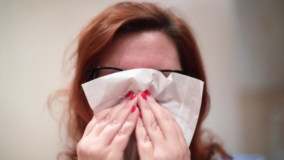 A woman holding a tissue to her nose