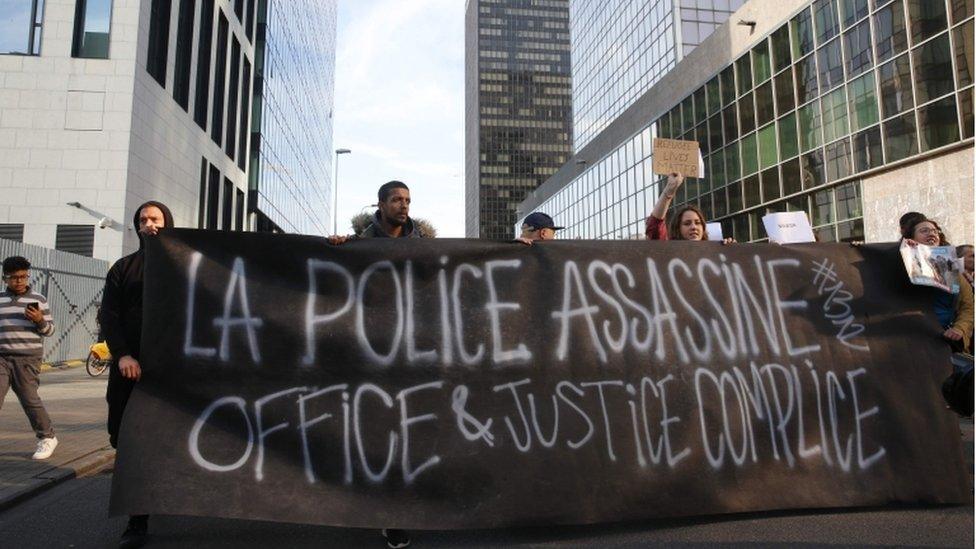 Activists hold a large banner condemning the police as they protest in front of the immigration office in Brussels