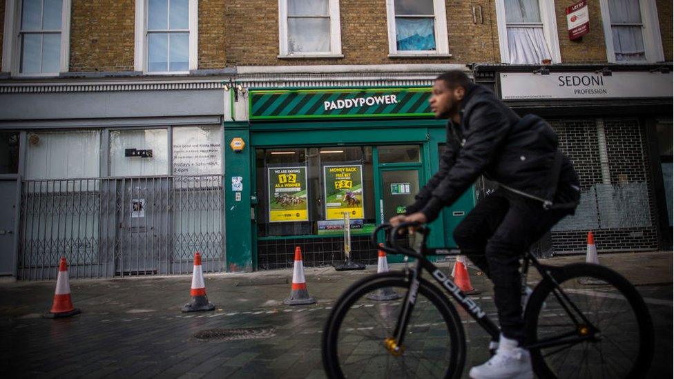 A young man rides a bicycle past a betting shop