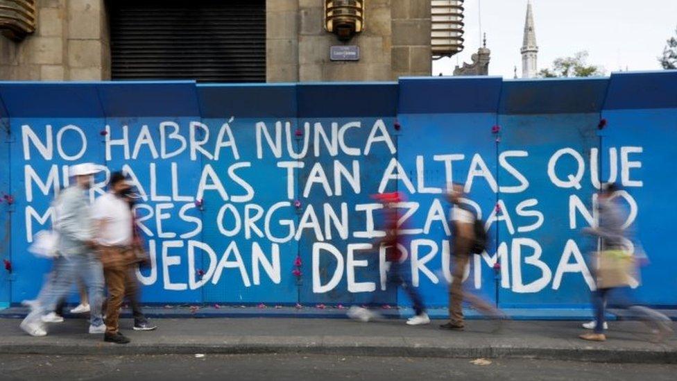 People walk past a barricade with a slogan reading "There will never be walls high enough that organised women can't overthrow" in Mexico City, Mexico March 7, 2021.