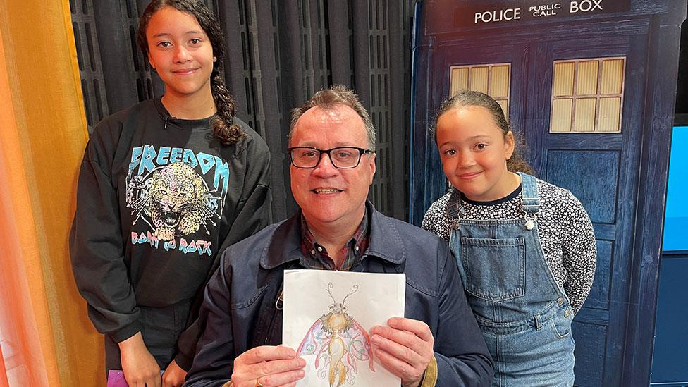 Newsrounders and sisters Mia and Talia with Doctor Who writer Russell T Davies, holding their drawing of a butterfly-like creature