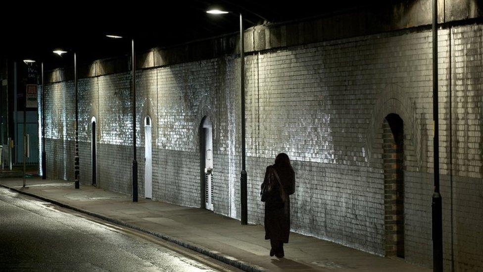 A woman walks alone along a street at night