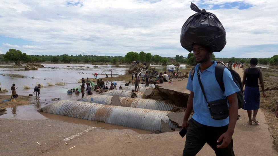 A man carries his ware as he walks past a cut-off road damaged by tropical storm Ana at Thabwa village, in Chikwawa district, southern Malawi