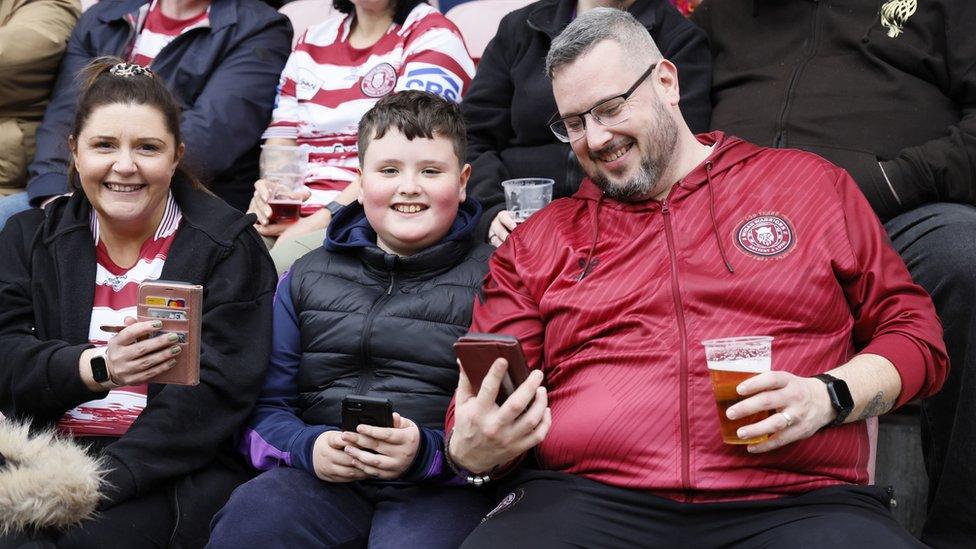 Fans check their phones for the emergency alert during the Betfred Super League match at the DW Stadium, Wigan