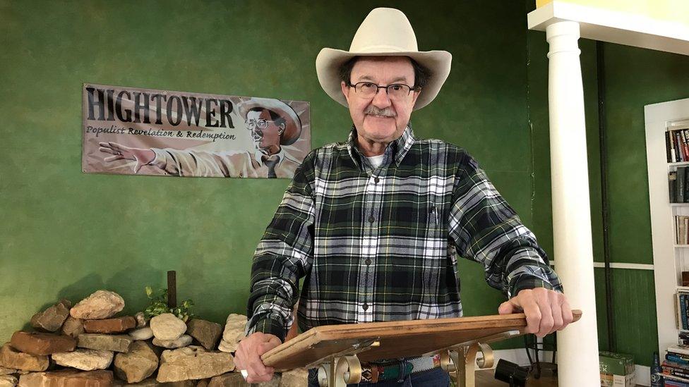 Jim Hightower smiles into the camera, wearing a chequered shirt and a cowboy hat