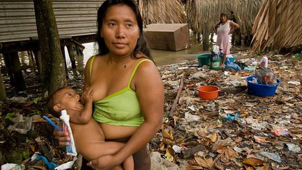 Warrau woman nursing child in a trash laden village on the shores of the Orinoco River in Venezuela.