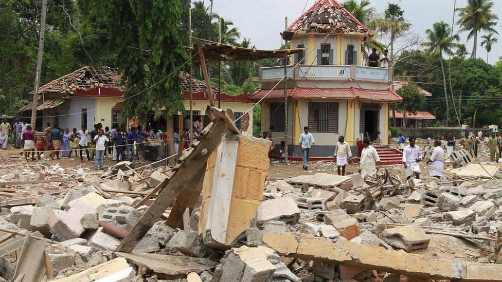 People stand next to debris after a broke out at a temple in Kollam in the southern state of Kerala, India