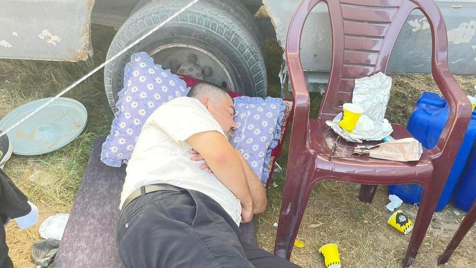 Adnan resting on a mattress by the wheel of a truck in Khan Younis