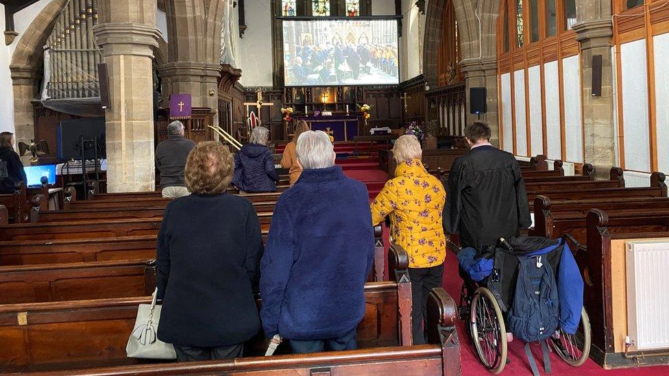 View from behind of people standing among pews