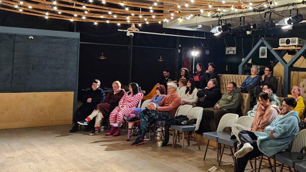 Audience members sitting down wearing pyjamas with rope lights above them