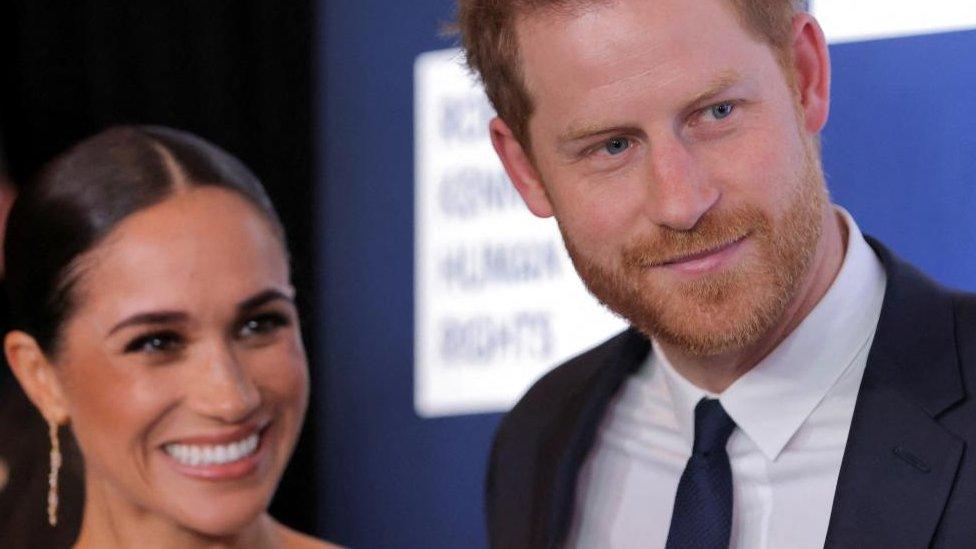 Meghan Markle and Prince Harry. They are both smiling and appear to be looking at someone just out of shot.