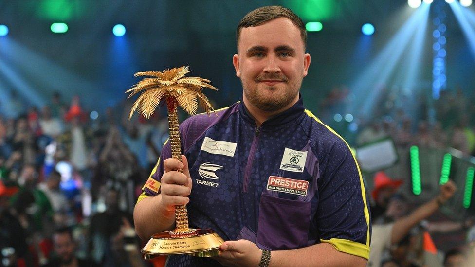 luke littler holding his bahrain darts masters trophy