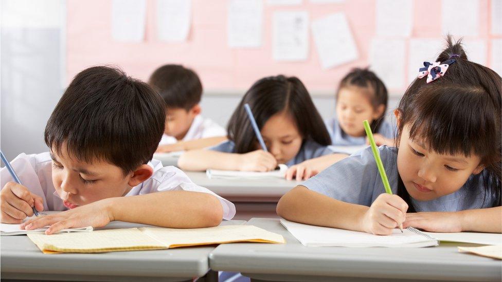 Group Of Students Working At Desks In Chinese School Classroom - stock photo