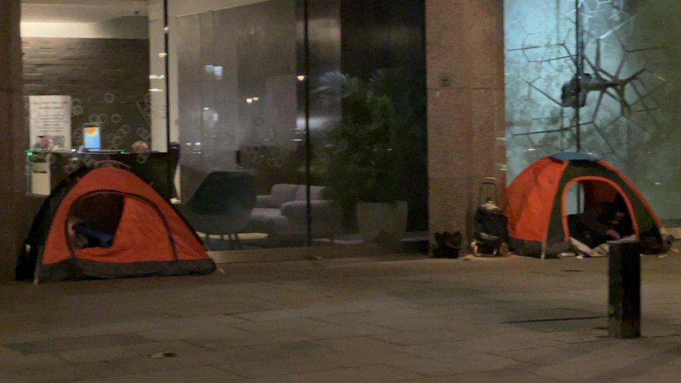 Two orange tents and some belongings on a street next to an office in central London.