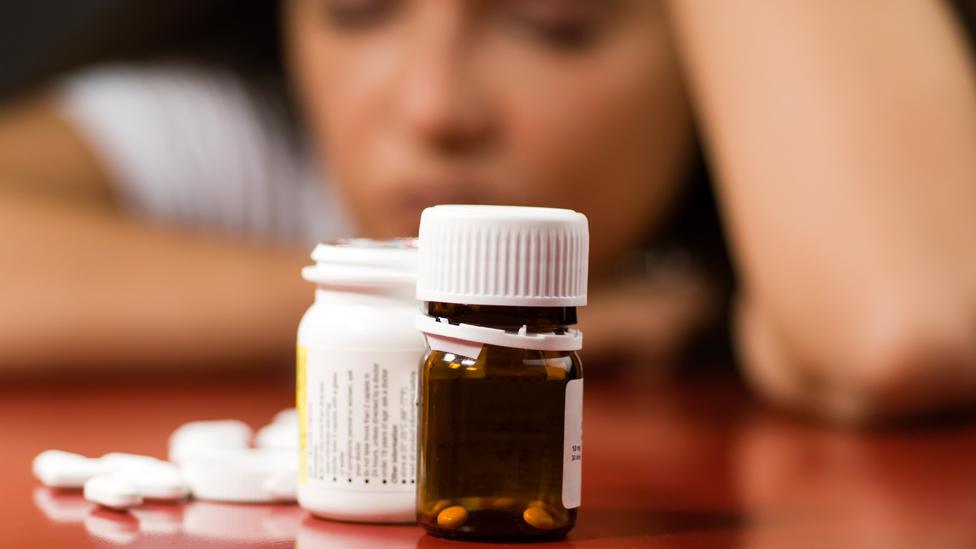 A woman looks at a bottle of pills