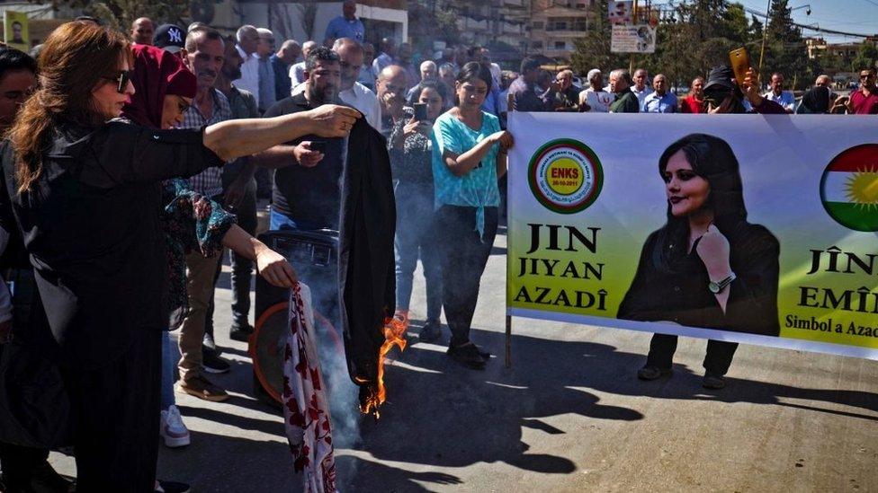 A woman burns a headscarf at a demonstration in north-eastern Syria