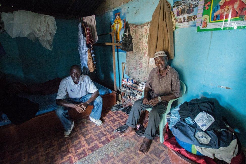 Two men sit inside their house smiling for the camera