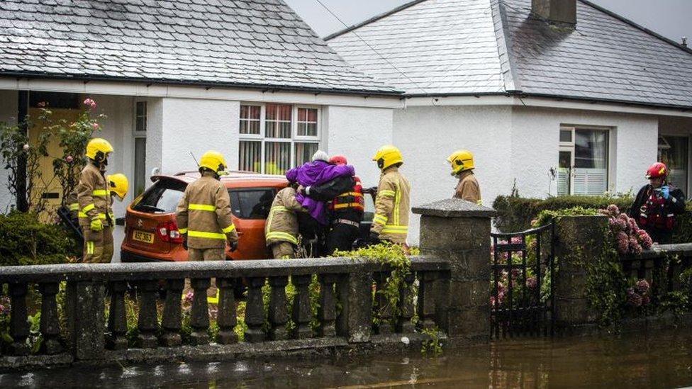 A group of firefighters helping a woman from her home