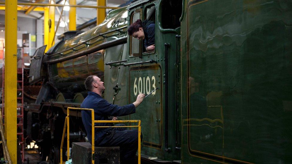 A workman paints the number 60103 on the cab of the Flying Scotsman while being watched by his daughter and colleague