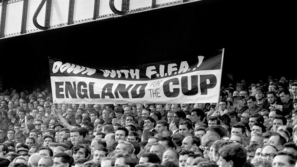 Liverpudlian England fans in the crowd at a 1966 World Cup match express their displeasure with Fifa after the governing body switched England's semi-final match from Goodison Park to Wembley